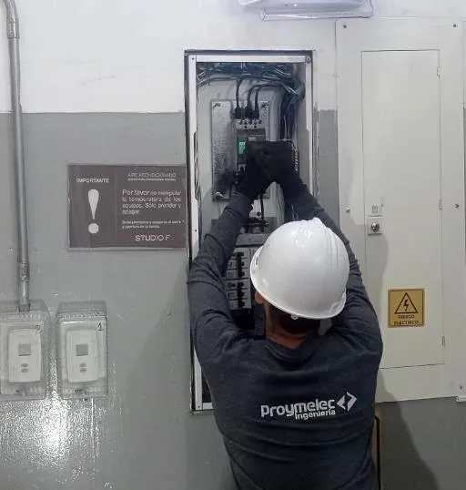 Técnico de Proymelec con casco y guantes trabajando en un tablero eléctrico
