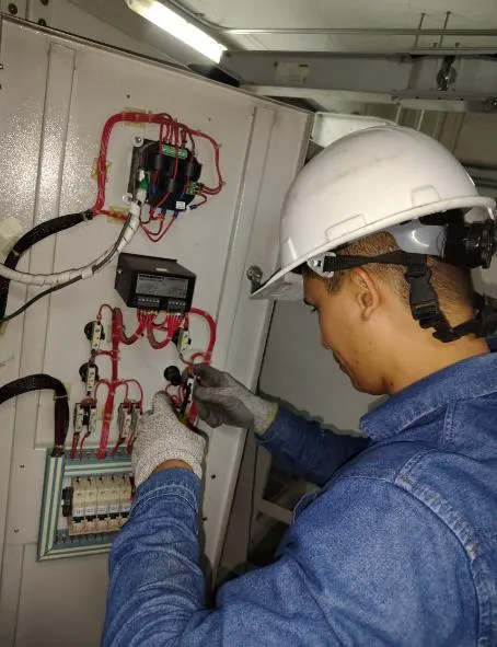 Técnico con casco y guantes trabajando en un tablero de control